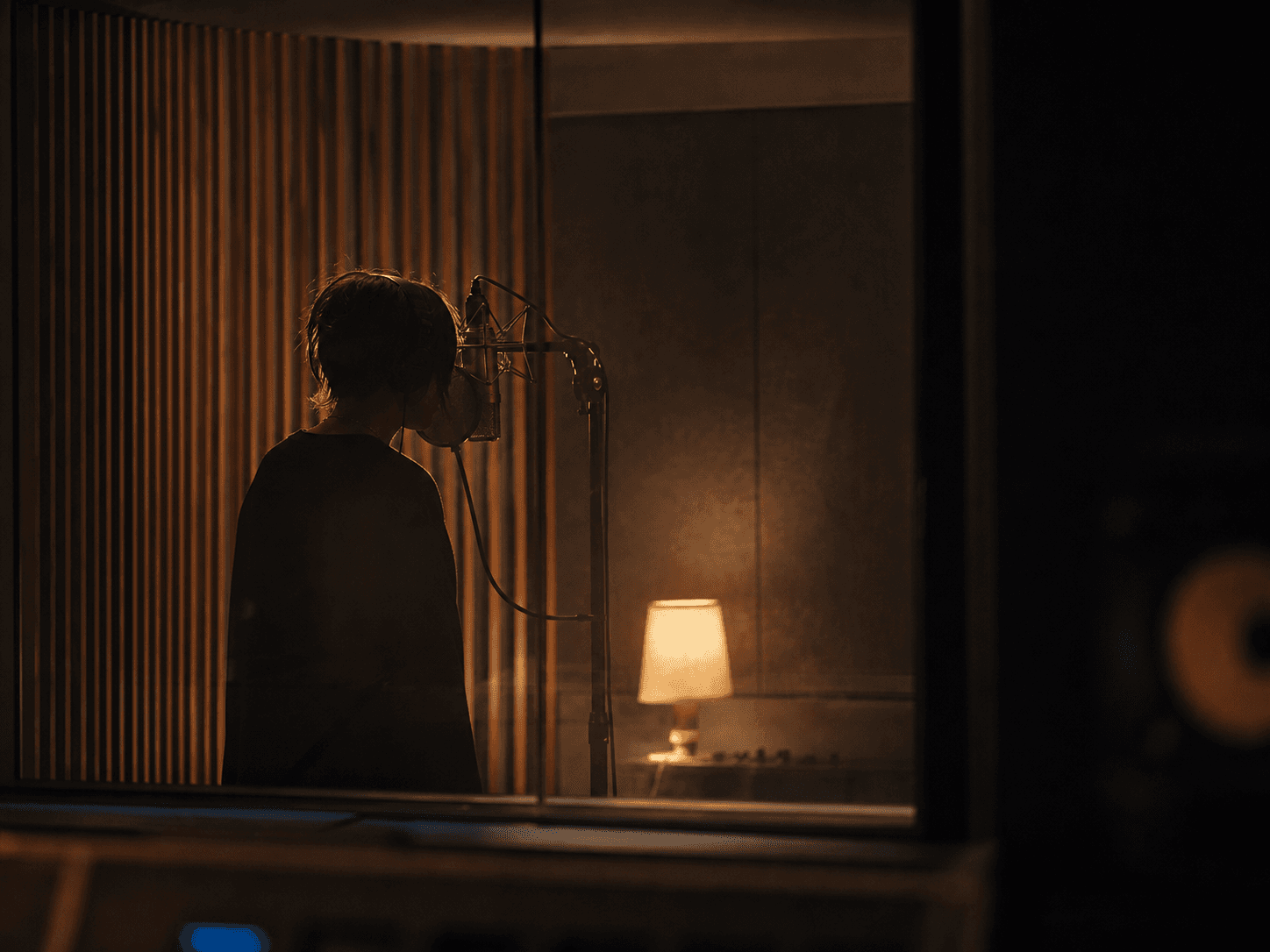 A vocalist recording an intimate take in a dark wood-lined studio